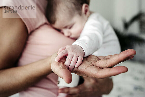 Hand of mother holding baby girl's hand at home