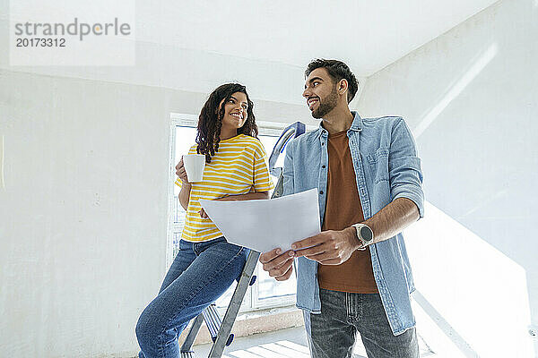 Glückliches junges Paar diskutiert mit Bauplan im neuen Zuhause