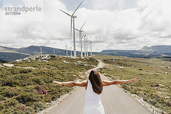 Spain  Madrid  Back of woman standing with raised arms in middle of road stretching past wind farm