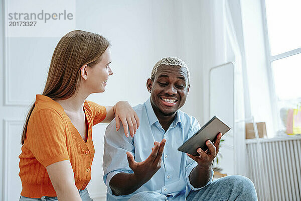 Glücklicher junger Mann diskutiert und hält Tablet-PC mit Frau zu Hause