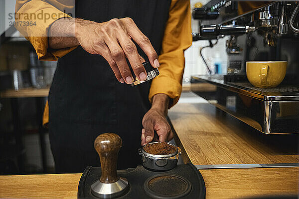Barista stampft gemahlenen Kaffee im Siebträger mit Tamper im Café
