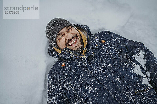 Cheerful mature man lying on snow at park