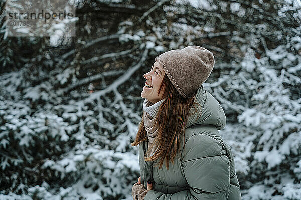 Fröhliche Frau  die im Winter in der Nähe von Bäumen lacht