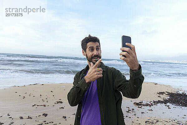 Mann gestikuliert und spricht per Videoanruf über sein Smartphone am Strand