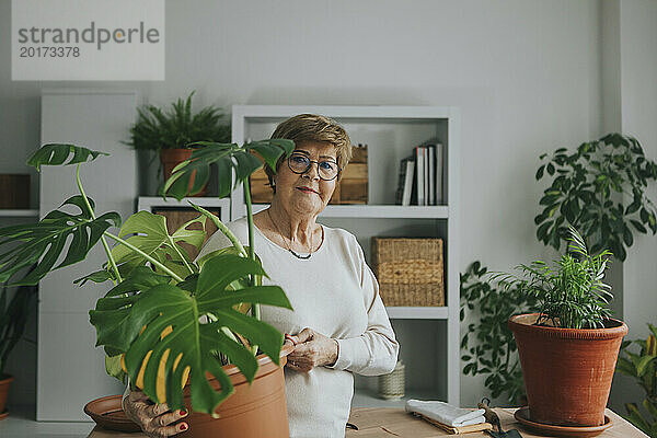 Lächelnde Frau hält Monstera-Blumentopf zu Hause