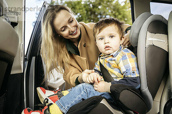 Lächelnde Mutter passt den Sicherheitsgurt für ihren Sohn an  der im Auto sitzt