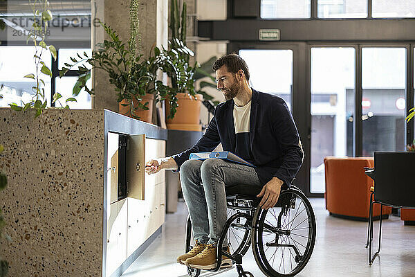 Geschäftsmann im Rollstuhl mit Behinderung öffnet Schrank am Arbeitsplatz