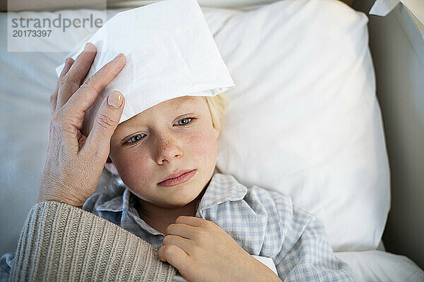 Nachdenklicher kranker Junge mit weißer Kompresse auf der Stirn zu Hause