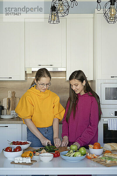 Teenage friends cutting vegetables in kitchen at home