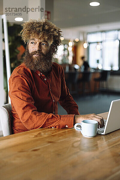 Reifer Geschäftsmann sitzt mit Laptop und Kaffeetasse in der Bürokantine