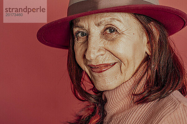 Lächelnde ältere Frau mit Hut vor rotem Hintergrund