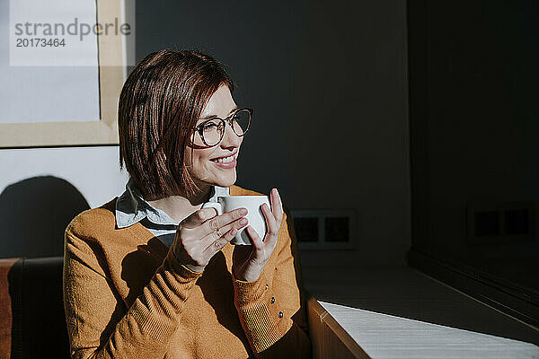 Smiling woman holding coffee cup and enjoying sunlight