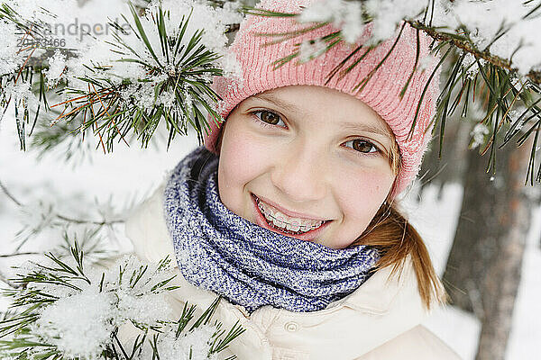 Lächelndes Mädchen mit Zahnspange in der Nähe schneebedeckter Äste