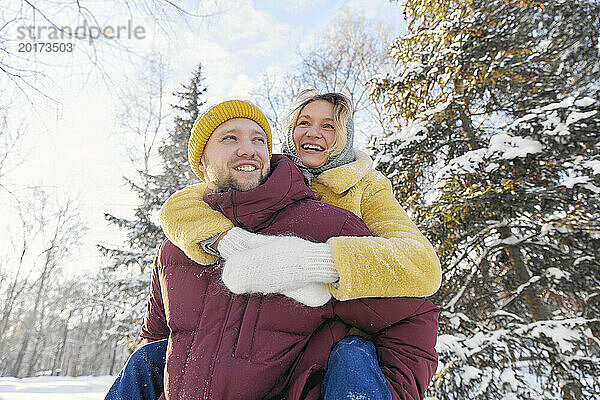 Glücklicher Mann gibt einer jungen Frau im Winterwald eine Huckepackfahrt