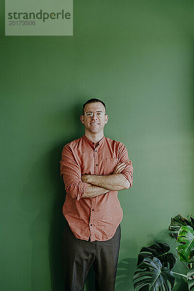 Lächelnder Mann steht mit verschränkten Armen vor einer grünen Wand