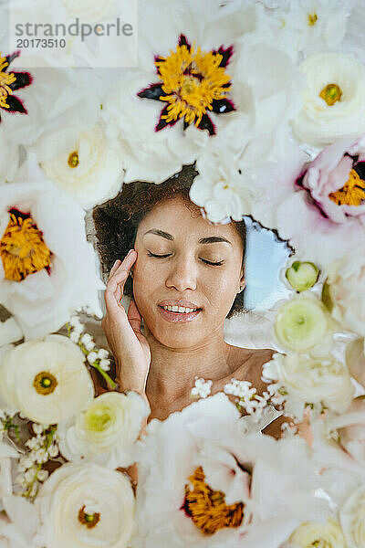 Junge Frau mit geschlossenen Augen liegt unter einer Glasoberfläche mit Blumen