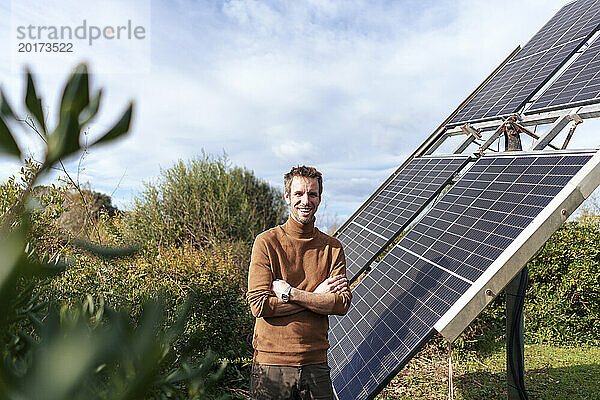 Lächelnder Mann  der an einem sonnigen Tag in der Nähe von Sonnenkollektoren steht