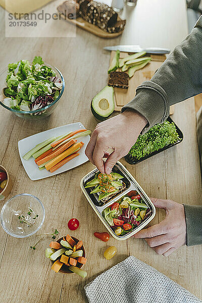 Junger Mann garniert Mikrogrün über vegetarisches Essen in der Lunchbox