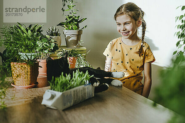 Happy girl with cat on table near potted plants at home