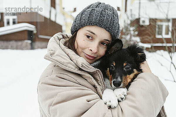 Frau trägt Strickmütze und umarmt Hund im Winter