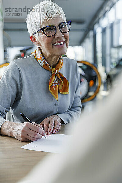 Glückliche ältere Frau  die am Schreibtisch Papierkram erledigt