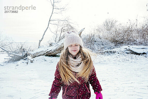 Lächelndes Mädchen mit geschlossenen Augen  das im Winter auf Schnee steht