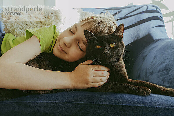 Lächelnder Junge mit geschlossenen Augen  der zu Hause mit der Katze auf dem Sofa liegt