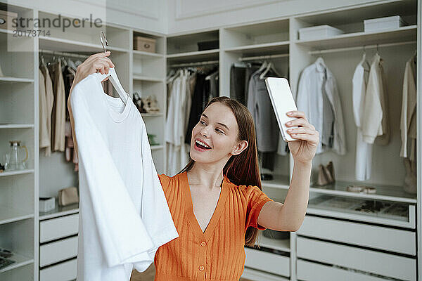 Glückliche junge Frau  die zu Hause ein Selfie mit T-Shirt über ihr Smartphone macht