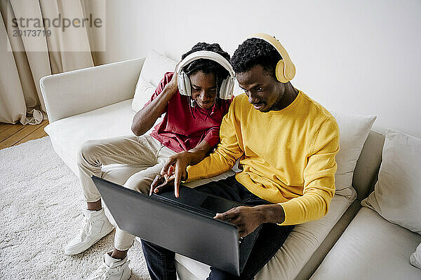 Junge Freunde tragen kabellose Kopfhörer und benutzen zu Hause einen Laptop