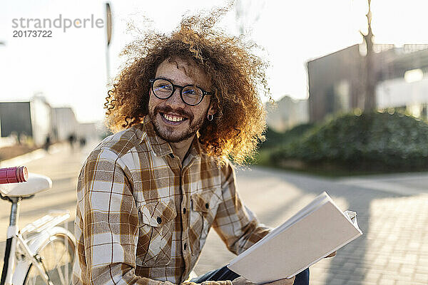 Glücklicher Mann  der mit einem Buch auf der Straße sitzt