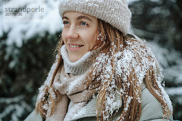 Lächelnde Frau mit Schnee auf braunem Haar im Winter