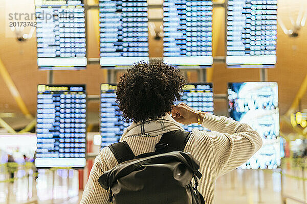 Mann mit lockigem Haar blickt auf die Ankunfts- und Abflugtafel am Flughafen