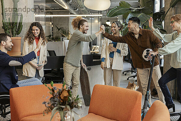 Fröhliche  vielfältige Kollegen  die sich bei Besprechungen im Büro gegenseitig High-Five geben