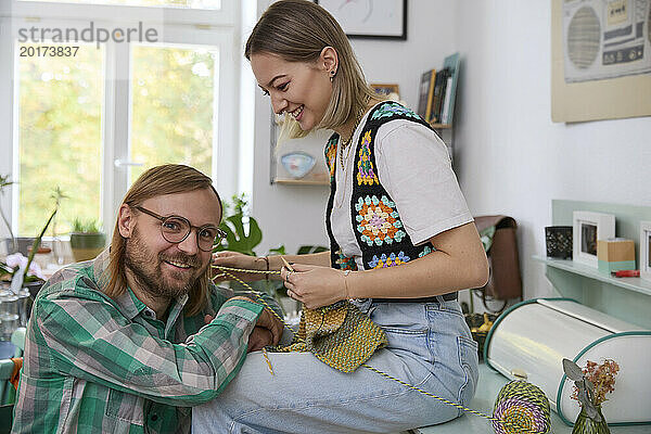 Lächelnde Frau strickt neben Mann  der zu Hause sitzt