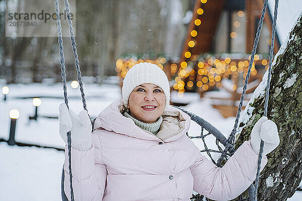 Lächelnde reife Frau  die im Winter auf einer Schaukel sitzt