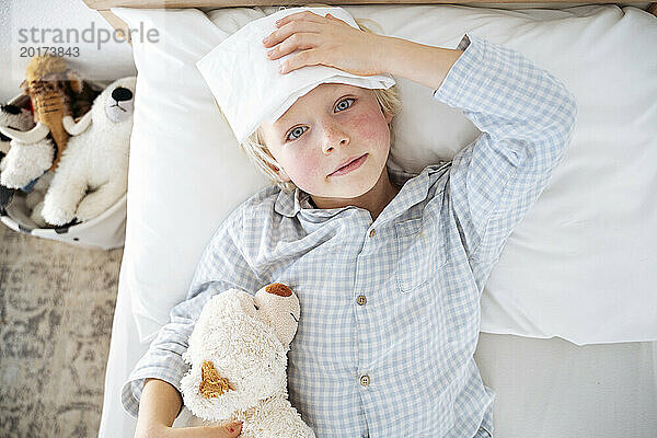 Kranker Junge liegt zu Hause mit Kompresse über der Stirn im Bett