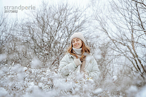 Lächelnde Frau in warmer Kleidung inmitten gefrorener Bäume im Winter