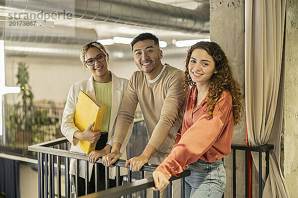 Lächelnde junge Geschäftskollegen lehnen sich im Büro an das Geländer