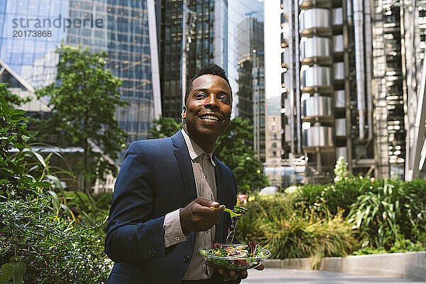 Glücklicher reifer Geschäftsmann sitzt mit einer Schüssel Salat im Büropark
