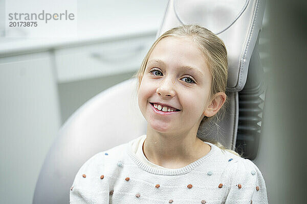 Lächelndes Mädchen sitzt auf dem Zahnarztstuhl in der Klinik