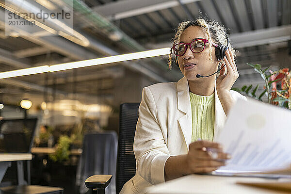 Junge Geschäftsfrau spricht über Headset und sitzt am Schreibtisch im Büro