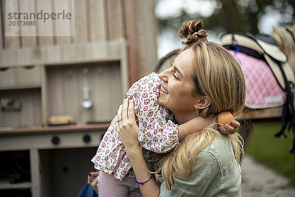 Glückliche Mutter umarmt Tochter neben Holzpferd