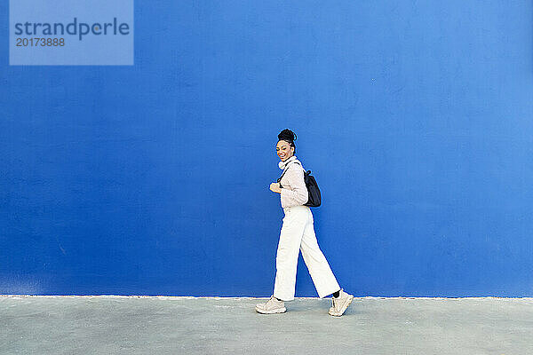 Glückliche Frau  die vor einer blauen Wand läuft