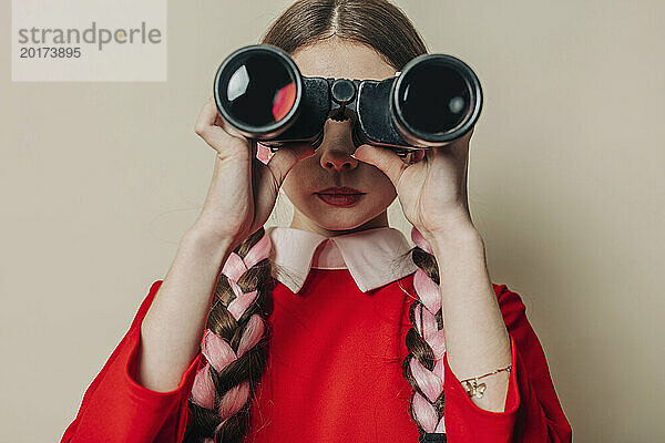 Junge Frau schaut durch ein Fernglas vor der Wand