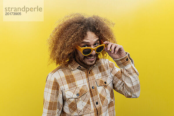 Glücklicher Mann mit Sonnenbrille und stehend vor gelber Wand
