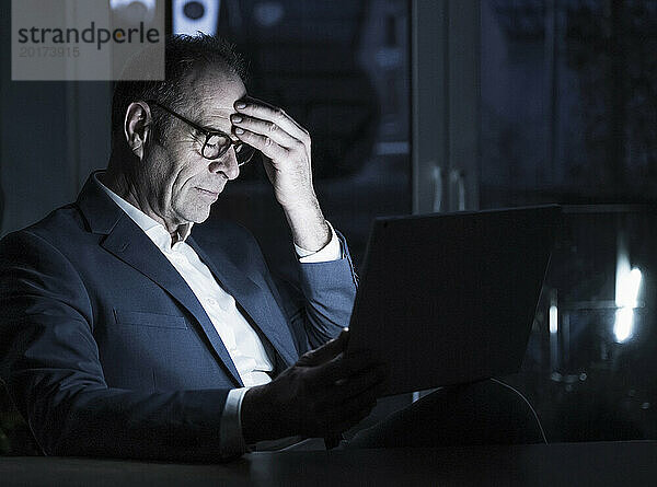 Erschöpfter Freiberufler reibt sich im Heimbüro den Kopf neben dem Laptop