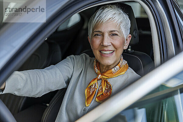 Glückliche ältere Frau mit grauen Haaren sitzt im Auto