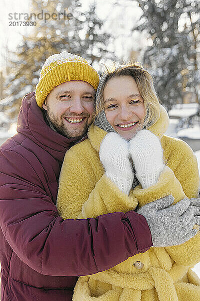 Lächelnder Mann umarmt Frau im Winterwald