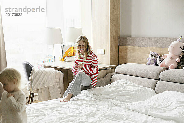 Lächelndes Mädchen  das zu Hause neben dem Bett sitzt