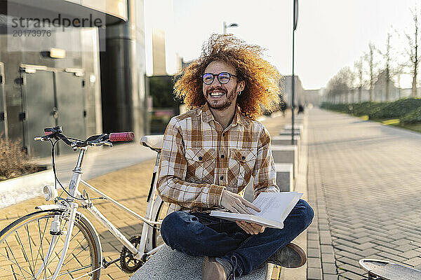 Lächelnder Mann mit Buch sitzt auf einem Sitz neben dem Fahrrad